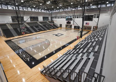 New School gymnasium with grey telescoping bleachers and retractable basketball hoops from BROC