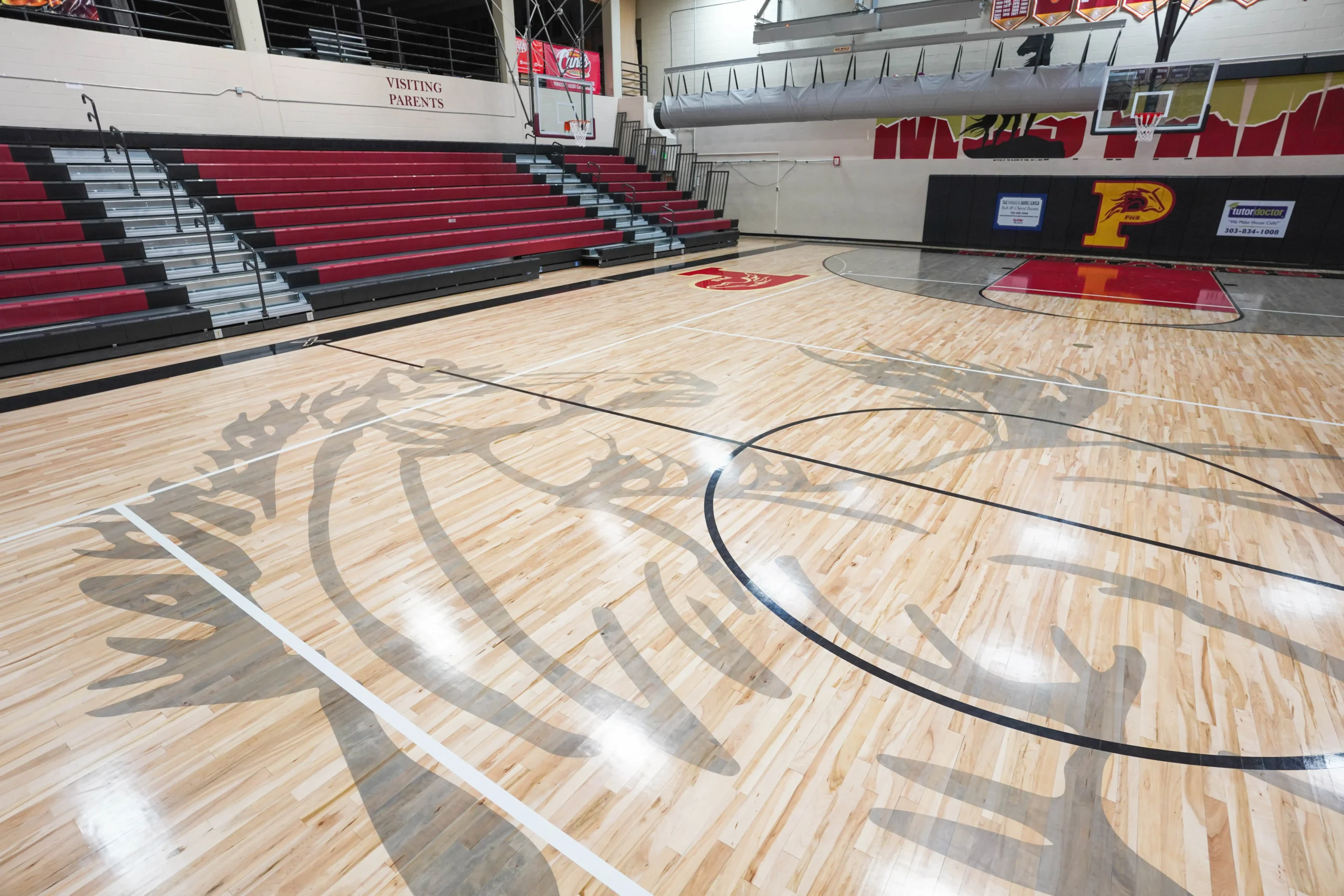 School gymnasium red bleachers with maple floor and grey hoarse graphics and gym equipment installed by BROC