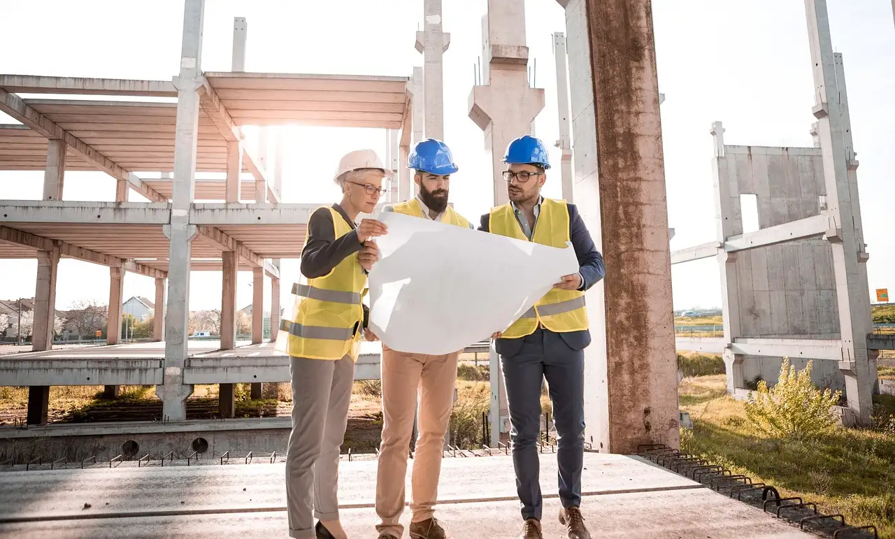 Image of architects with PPE on commercial job site looking at blueprints.